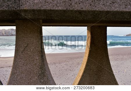 Waves Breaking Against A Beach With Sunset Light. View Through A Handrail In A Promenade. La Coruna,