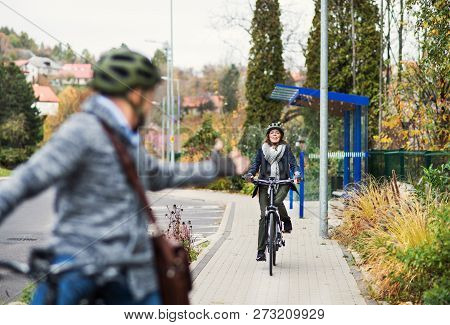 An Active Senior Couple With Electrobikes Cycling Outdoors On Pathway In Town.