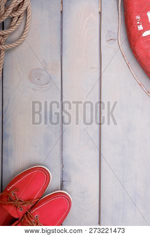 Red Boat Shoes On Wooden Background Near Lifebuoy And Rope. Top View. Copy Space
