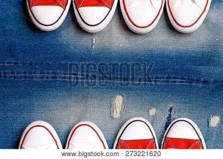 White And Red Sneakers On A The Ripped Denim Background.