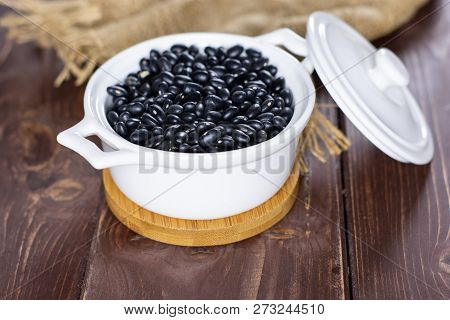 Lot Of Whole Raw Black Turtle Beans In A Ceramic Stewpan On Brown Wood