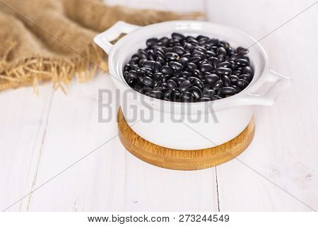 Lot Of Whole Raw Black Turtle Beans In A Ceramic Stewpan On White Wood