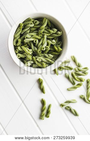 Uncooked spinach gemelli pasta in bowl.