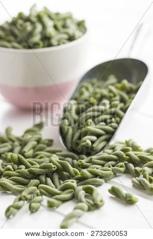 Uncooked spinach gemelli pasta in scoop.