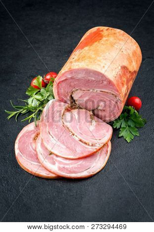 Traditional Allgauer veal roast roll sausage sliced and as piece with tomatoes and chili as closeup on a slate slab