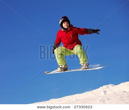 Snowboardista skoky vzduchem s tmavě modrou oblohou v pozadí