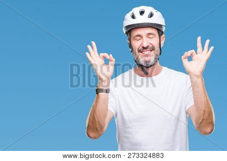Middle age senior hoary cyclist man wearing bike safety helment isolated background relax and smiling with eyes closed doing meditation gesture with fingers. Yoga concept.