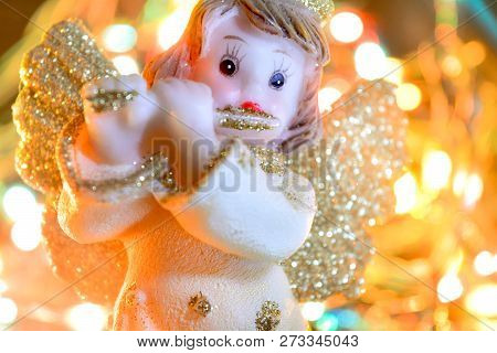 Figurine Of Little Angel With Golden Shiny Wings And Halo That Plays Flute On Shining Background Of 