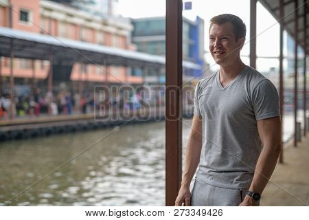 Young Happy Tourist Man Thinking While Waiting At The Local Pier In Bangkok