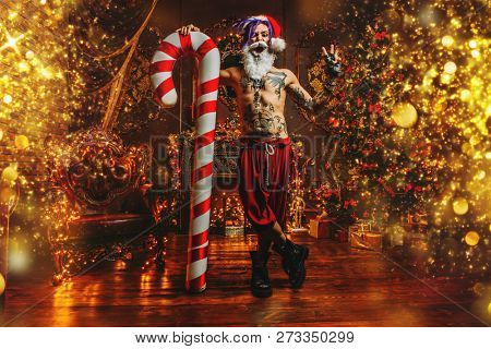 Bad Santa concept. Portrait of a nude tattooed Santa with purple dreads demonstrating antisocial behavior, rudeness and aggression. 