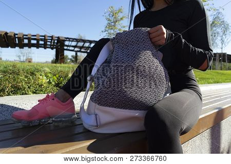 Woman Rummaging In Backpack After Exercising Outdoors In Urban Environment.