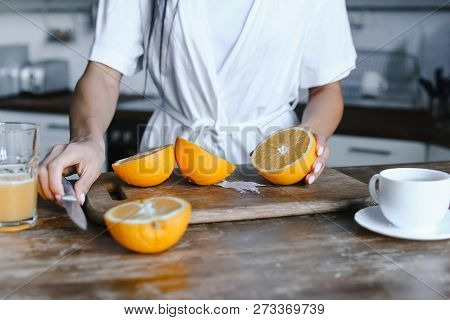 Cropped Image Of Mixed Race Girl In White Robe Preparing Orange Juice In Morning And Cutting Oranges