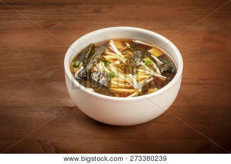 A Photo Of A Bowl Of Miso Soup With Tofu, Scallions, Noodles, Wakame Seaweed And Enoki Mushrooms On 
