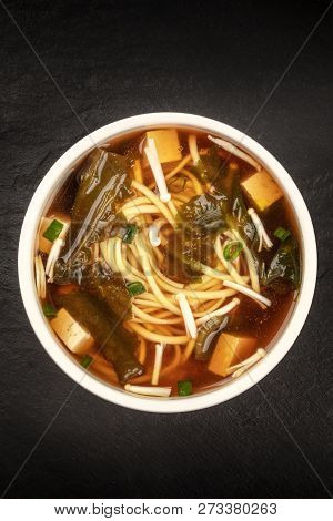 A Bowl Of Miso Soup With Tofu, Scallions, Noodles, Wakame, And Enoki Mushrooms, Shot From The Above 