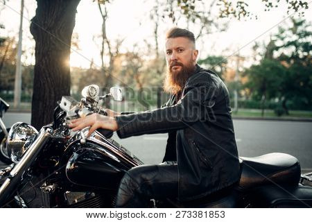 Baerded biker poses on chopper leaning on a helmet