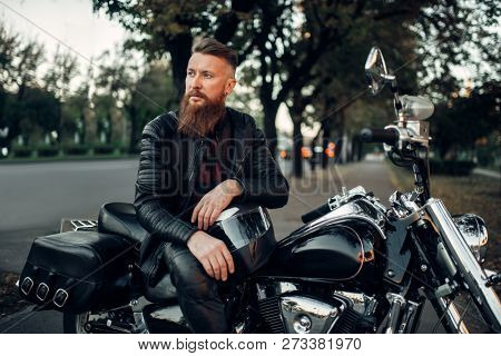 Baerded biker poses on chopper leaning on a helmet