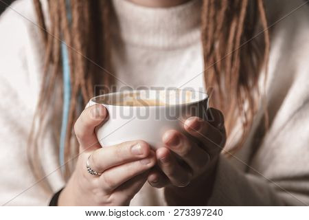 A White Cup Of Hot Latte Art Coffee With A Heart Shape In The Hands Of A Young Girl With Dreadlocks.