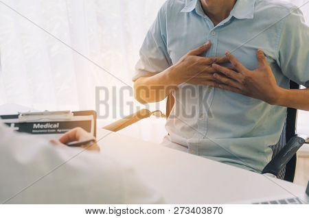 Young Man Hands On His Chest Suffering From Heart Attack Meet Doctor Writing Prescription On Clipboa