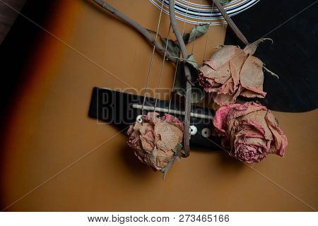 Acoustic Guitar With Dried Roses On The Wooden Table. Template For Advertising A Concert Of Memory S