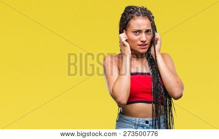 Young braided hair african american with pigmentation blemish birth mark over isolated background covering ears with fingers with annoyed expression for the noise of loud music. Deaf concept.