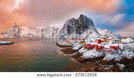 Panorama of famous tourist attraction Hamnoy fishing village on Lofoten Islands, Norway with red rorbu houses. With falling snow in winter on sunrise