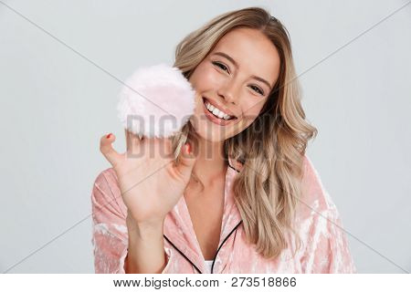 Pretty young girl wearing pajamas holding powder puff, isolated over gray background