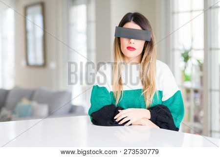 Young beautiful woman blindfold eyes with black censor band at home with serious expression on face. Simple and natural looking at the camera.