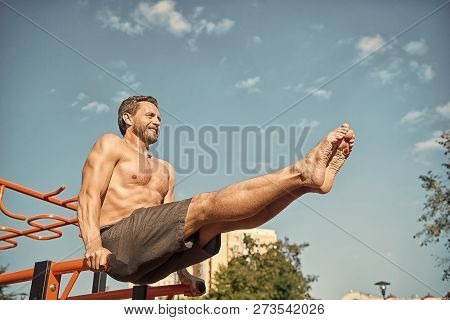 Sportsman Exercising On Parallel Bars Outdoors On Blue Sky. Man Training Abs By Raising Legs. Athlet