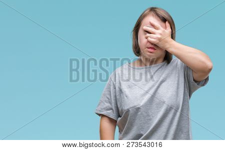 Young adult woman with down syndrome over isolated background peeking in shock covering face and eyes with hand, looking through fingers with embarrassed expression.