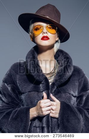 Gorgeous blonde woman posing in luxurious fur coat and a hat. Fashion, beauty. Studio shot.