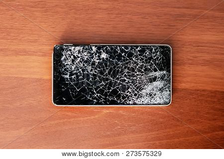 Modern Frameless Smartphone With Broken Screen On The Wooden Table. Phone Repair Concept. Old Broken