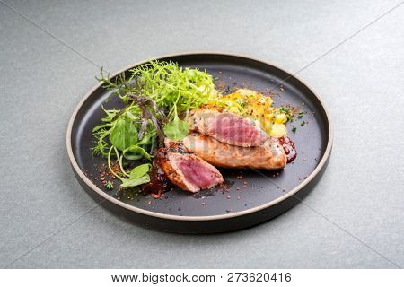 Fried suckling pig fillet with potatoes and lettuce offered as closeup in a modern design plate with spicy sauce  