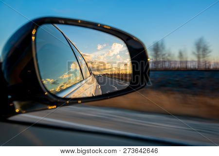 Driving A Car On An Autumn Road With Clouds In The Rear View Mirror