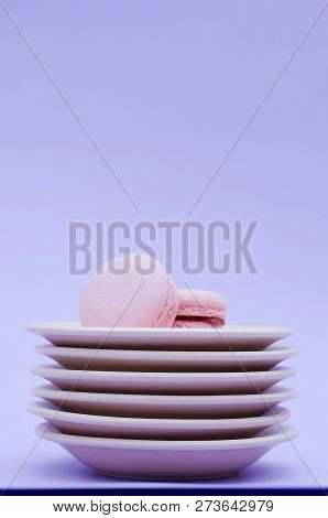 Two Macaroons On A Stack Of Beige Saucers On A Purple Background.