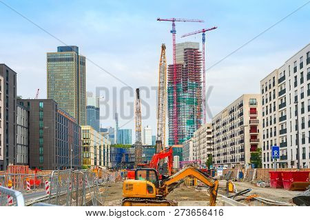 Excavator, Cranes And Construction Equipment At Construction Site In Downtown At Street With Buildin