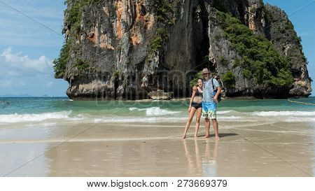 Father Standing In The Water On Tropical Island With Arm Around Daughter At Beach
