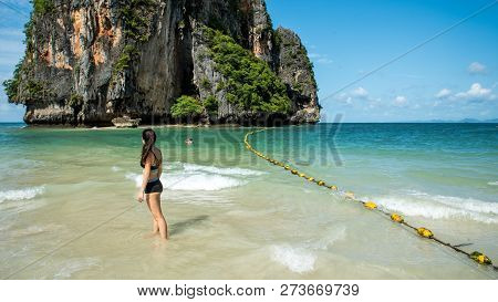 Teen Standing In Water On Tropical Beach Looking Away From Camera