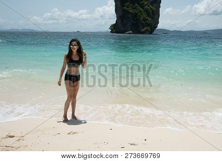 Young Girl Standing On Beach In Black Bathing Suit With Tropical Island In Background
