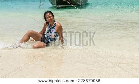 Asian Woman Sitting At Edge Of Beach In Water On Tropical Island