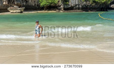 Woman In Hat And One Piece Bathing Suit Kneeling In Water On Trropical Island