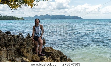Asian Woman In Bathing Suit Smiling And Standing On Rocks On Beach