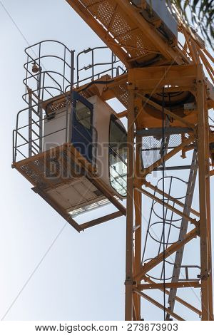 A Close Up View From The Ground Of The Drivers Cab Of A Yellow Crane Working On A Construction Site