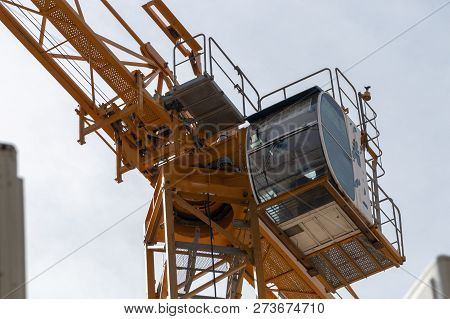 A Close Up View From The Ground Of The Drivers Cab Of A Yellow Crane Working On A Construction Site