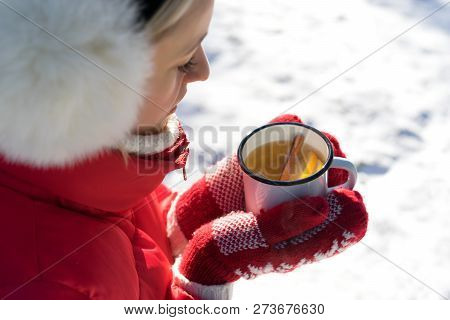 Hands In Knitted Mittens Holding Steaming Cup Of Hot Tea On Snowy Winter Morning Outdoors. Woman Hol