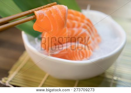 Chopsticks With Salmon Sashimi With Salmon Sashimi On Ice In With Bowl. Japanese Food In Asian Restu
