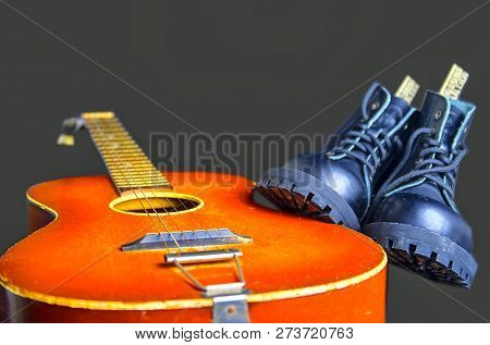 Rock And Roll Concept. Black Boots And Acoustic Guitar. Rock And Roll Boots On Black Background.