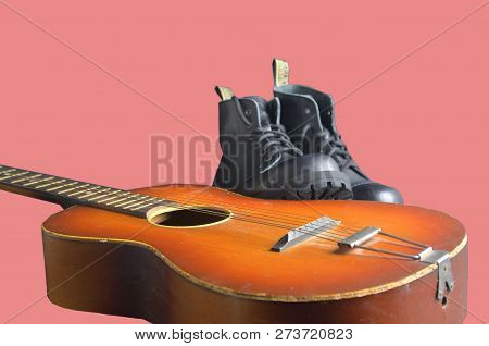 Rock And Roll Concept. Black Boots And Acoustic Guitar. Rock And Roll Boots On Pink Background.