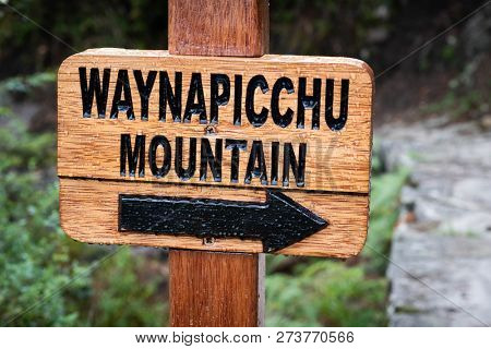 Closeup of wooden pointing sign with black label to Waynapicchu mountain coved with drops