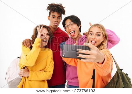 Group of cheerful teenagers isolated over white background, carrying backpacks, taking a selfie