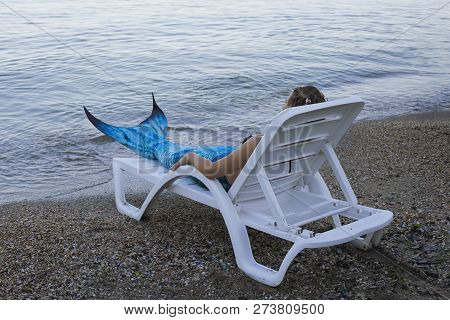 The Real Mermaid Is Reasting On The Sea Shore. Resting On A Sun Lounger. Blue Tail. The Body Is Cove